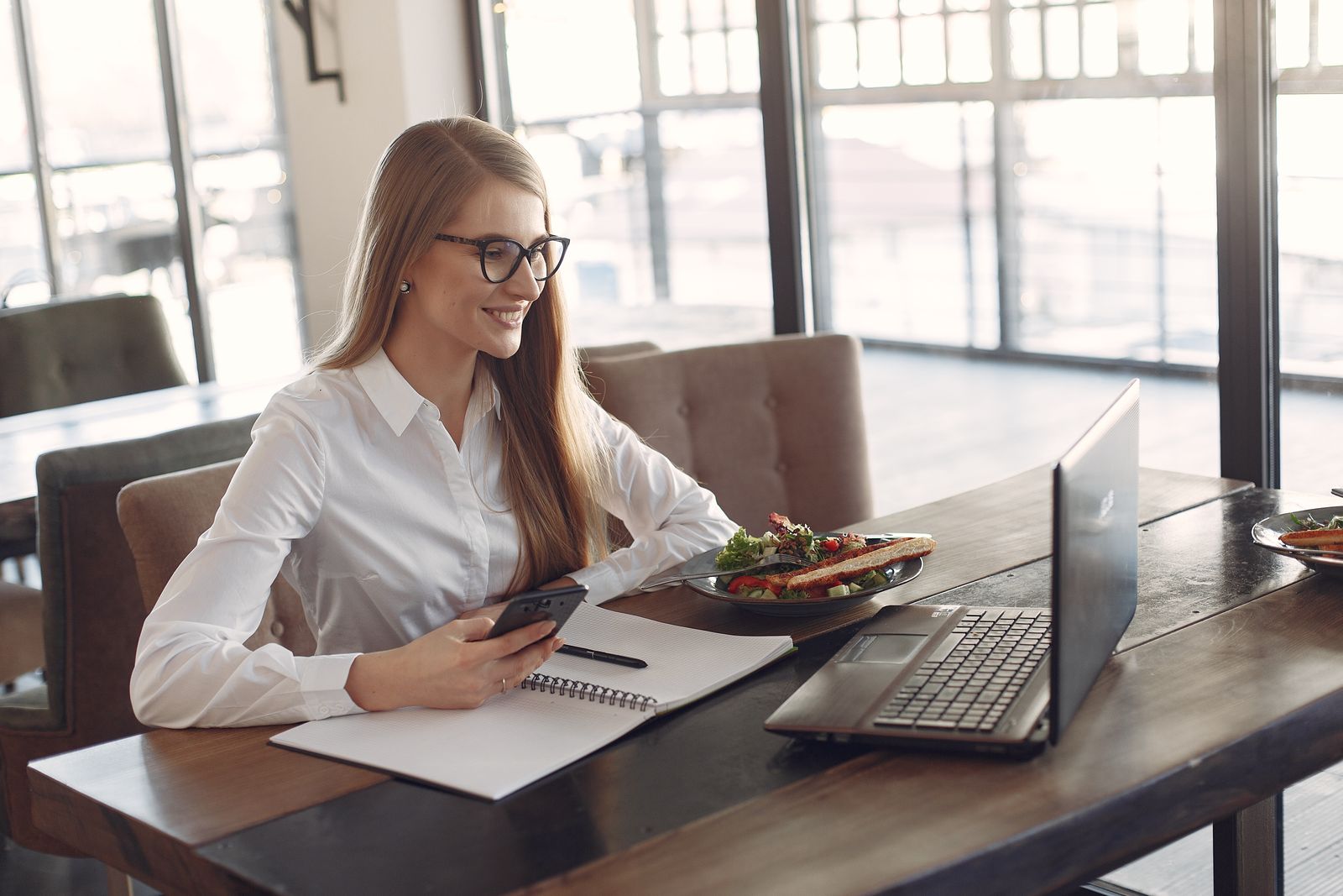A business owner checking messages on a phone next to an open laptop